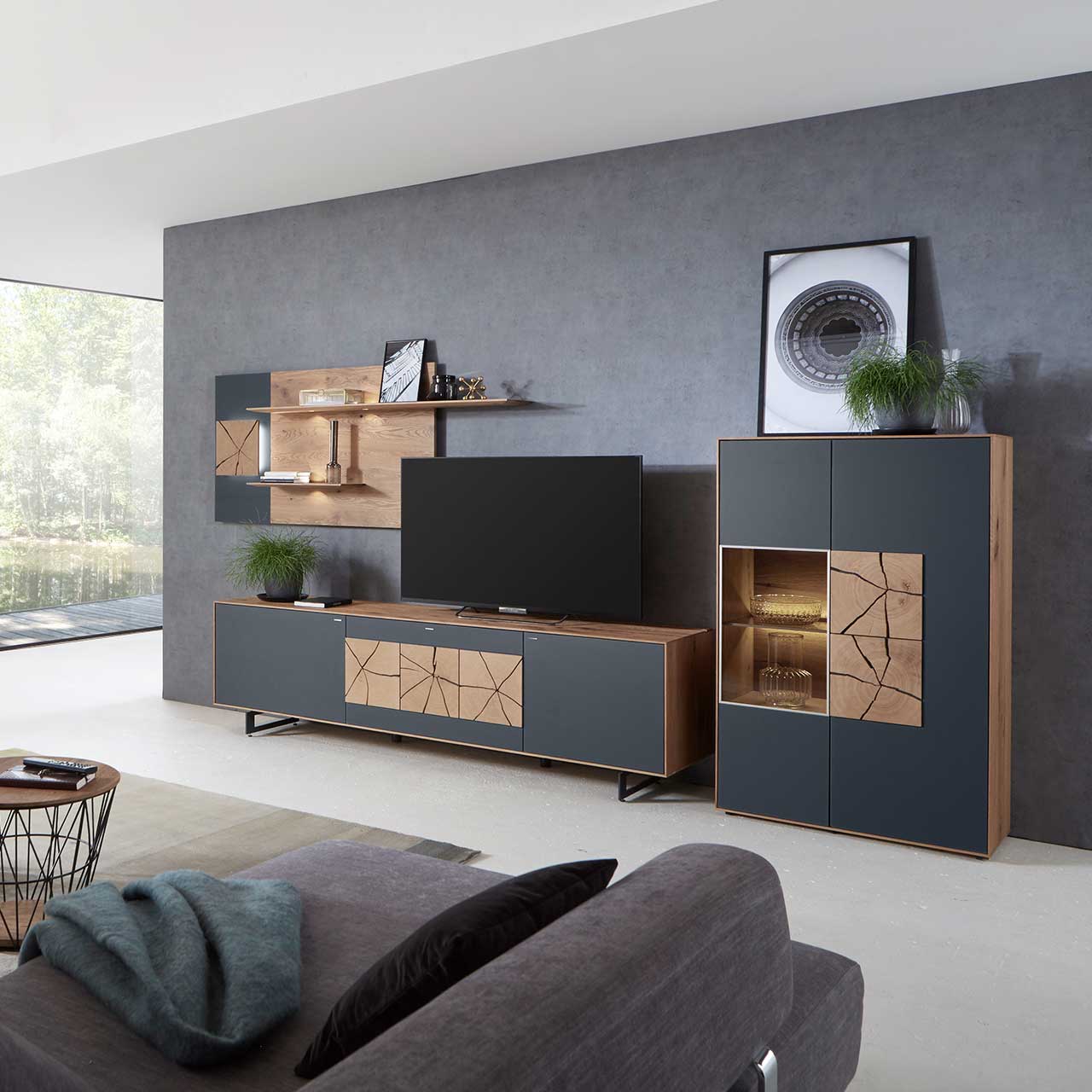 Wohnzimmer mit moderner dreiteiliger Massivholz Wohnwand mit Mattglas Anthrazit Fronten und dekorativen Hirnholzscheiben: Langes Lowboard mit Hirnholz und Kufen, Wandpaneel mit Regalböden, Highboard mit beleuchtetem Glasausschnitt und Hirnholz.