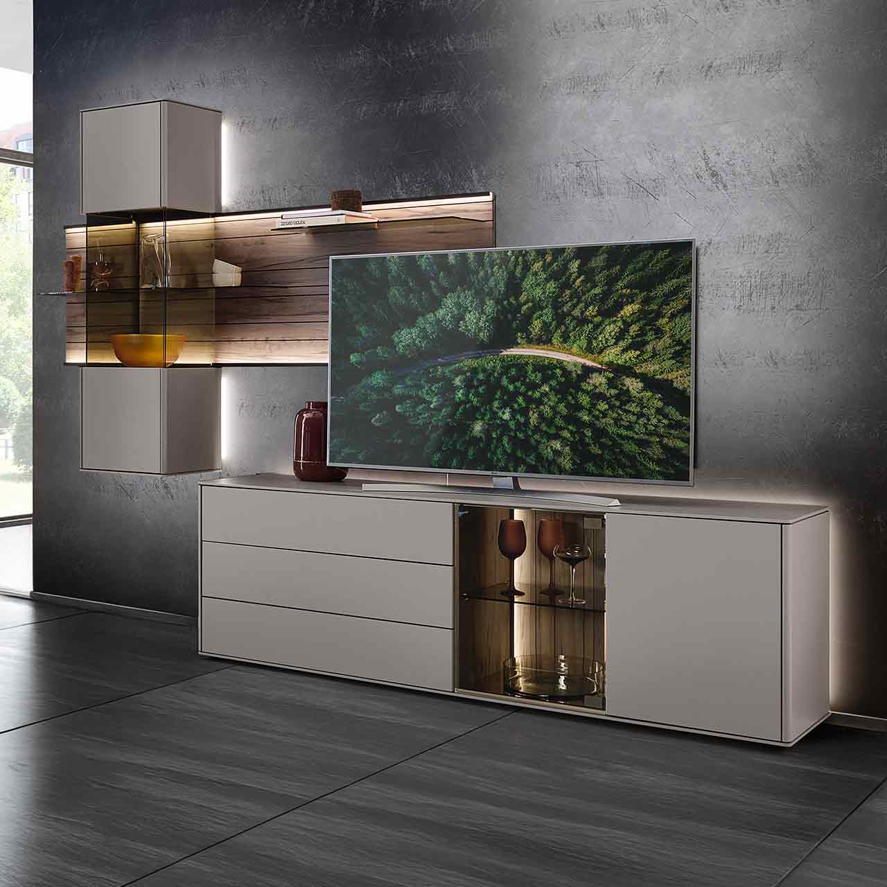 Hartmann AUDRA 5610 - Wohnwand Nr. V28 - dreiteilig aus Altholzbuche Uyaa und Lack Sand Modernes Wohnzimmer mit dreiteiliger Wohnwand bestehend aus einem Lowboard mit Glasausschnitt und Hängevitrine in Lack Sand sowie einem beleuchtetem Wandpaneel aus Altholzbuche mit drei Glasböden - an dunkler Wand.