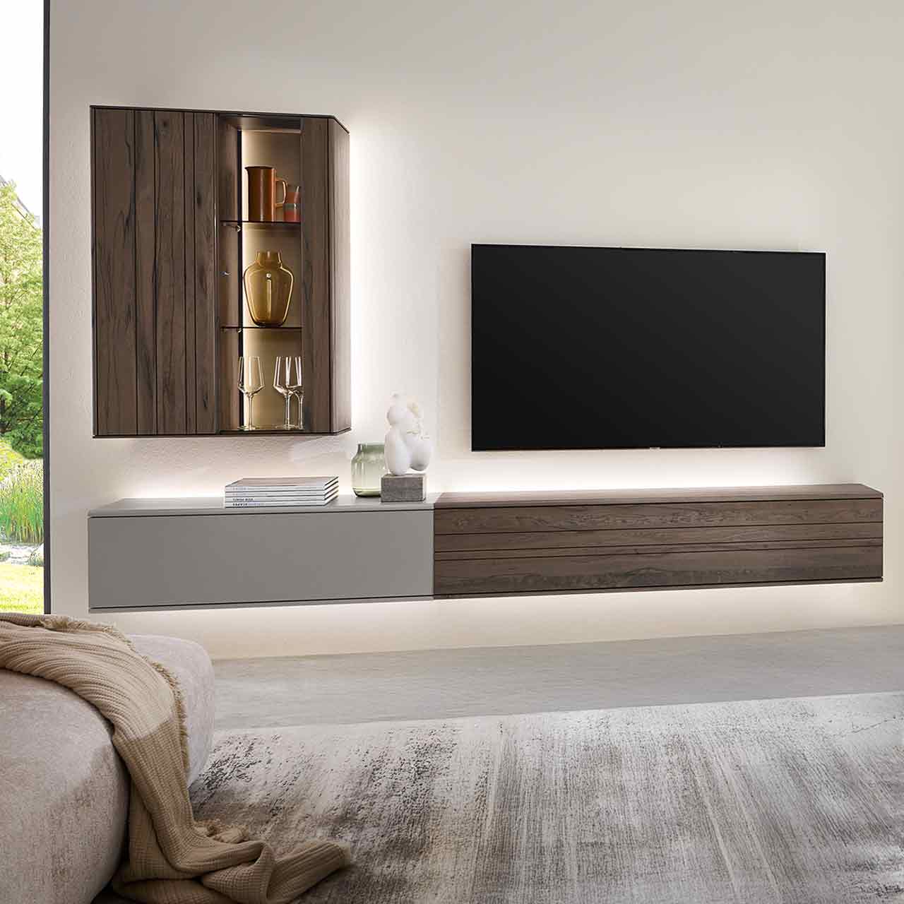 Hartmann AUDRA 5610 - Wohnwand Nr. V24 - dreiteilig aus Altholzbuche Uyaa und Lack Sand Moderne, dreiteilige Massivholzwohnwand bestehend aus zwei Hängelowboards in dunkelbraunem Holz und Lack sand und einer beleuchteten Hängevitrine in dunkelbraun mit sichtbarer Holzmaserung - an heller Wand.