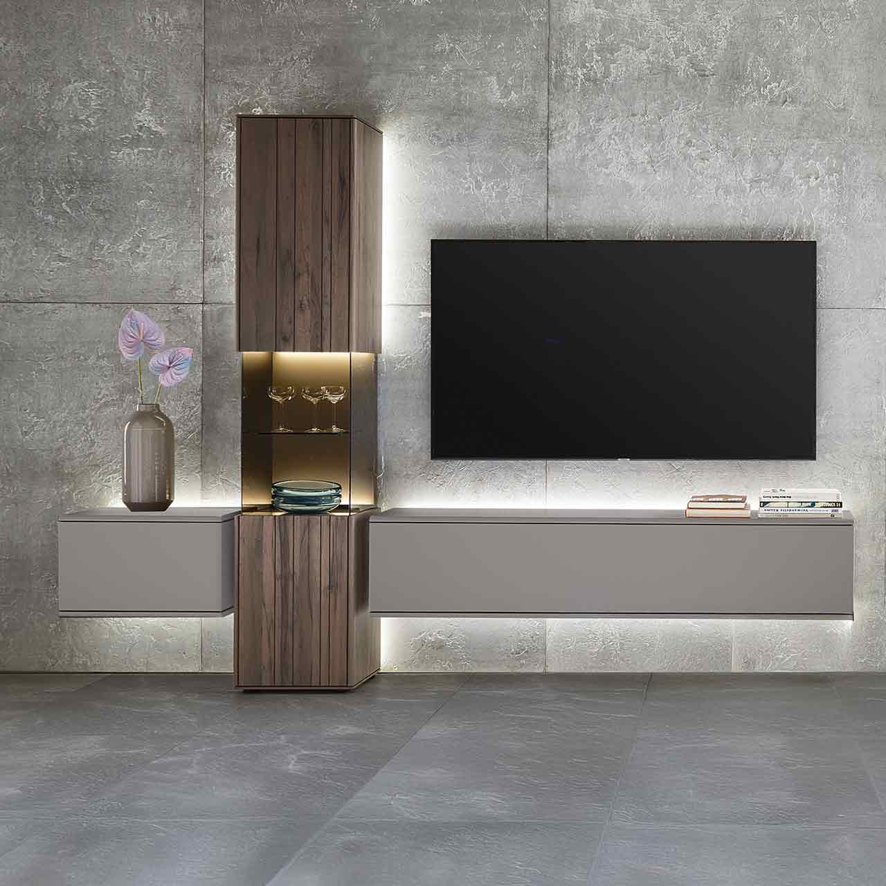 Hartmann AUDRA 5610 - Wohnwand Nr. V21- dreiteilig aus Altholzbuche Uyaa und Lack Sand Moderne, dreiteilige Massivholz-Wohnwand bestehend aus einer Standvitrine in dunkelbraunem Holz mit Maserung und beleuchtetem Glasausschnitt, rechts und links davon zwei Hängelowboards in Lack Sand.