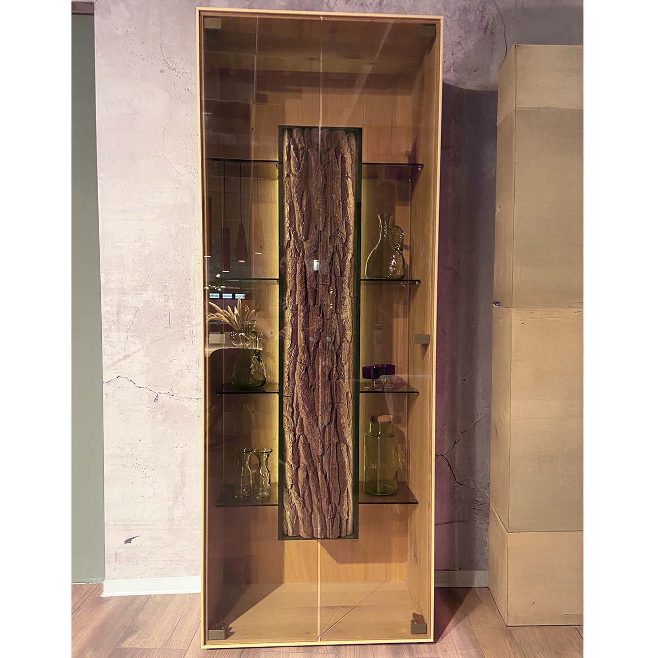 Moderne Standvitrine aus massiver Kerneiche Natur mit zwei Glastüren, innenliegenden Glasböden und mittigem Korpus mit beleuchteter Baumrinden-Applikation.