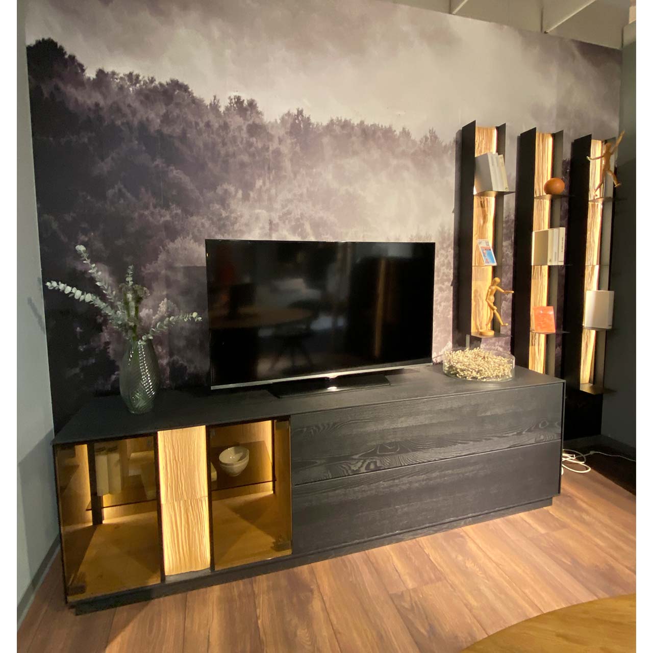 Moderne vierteilige Massivholz Wohnwand aus anthrazitfarbener Kernesche und hellem Spaltholz: Lowboard mit Glasausschnitt, Klappe und Schubkasten und dekorativem Spaltholz, drei Metallregale mit Ablageböden und beleuchteter Spaltholzrückwand.
