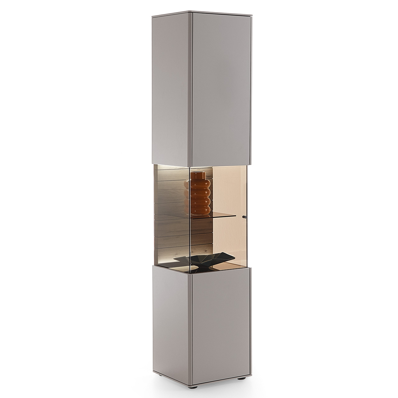 Hartmann AUDRA - Standvitrine 5610-0041 - Lack Sand - Türanschlag links Schmale moderne Standvitrine aus Massivholz mit sandfarben lackierten Fronten, mittig mit beleuchtetem Glasausschnitt und strukturierter Holzrückwand in dunkelbrauner Altholzbuche Uyaa.