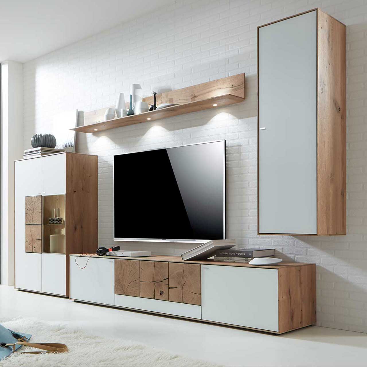 Wohnzimmer mit TV und moderner Massivholz Wohnwand aus Kerneiche Umato mit Mattglas weiß Fronten und rechteckigen Hirnholzscheiben: Hängeschrank, beleuchtetes Wandregal, Lowboard mit Hirnholz, Highboard mit Glasausschnitt und Hirnholz.