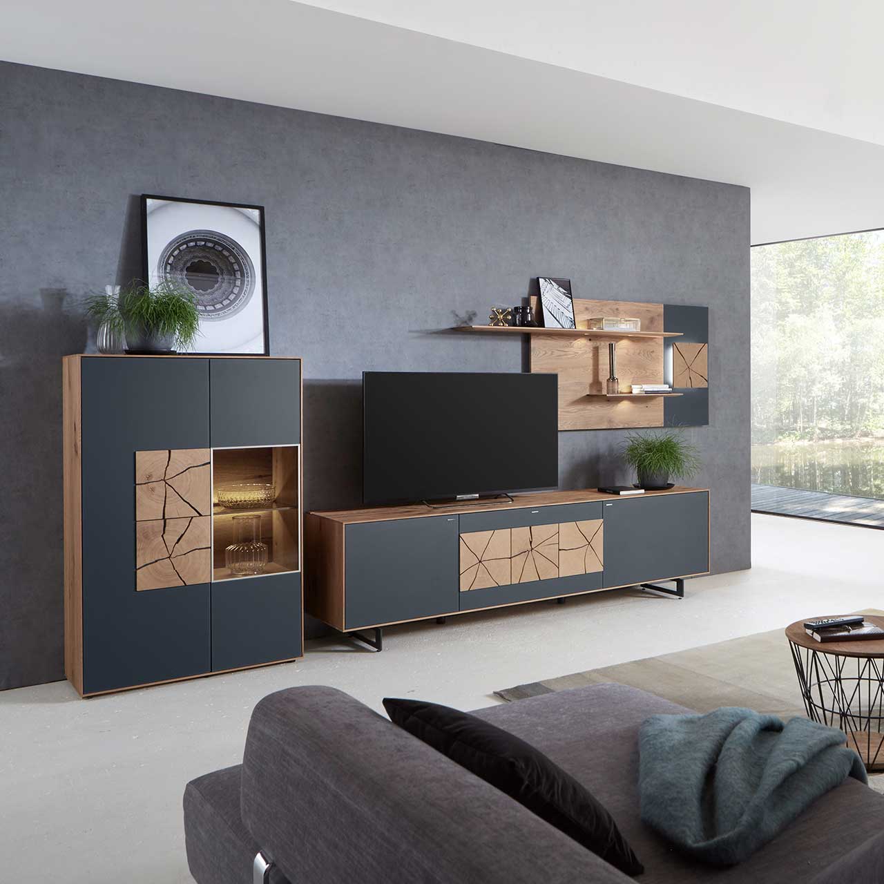 Wohnzimmer mit moderner dreiteiliger Massivholz Wohnwand mit Mattglas Anthrazit Fronten und dekorativen Hirnholzscheiben: Langes Lowboard mit Hirnholz und Kufen, Wandpaneel mit Regalböden, Highboard mit beleuchtetem Glasausschnitt und Hirnholz.