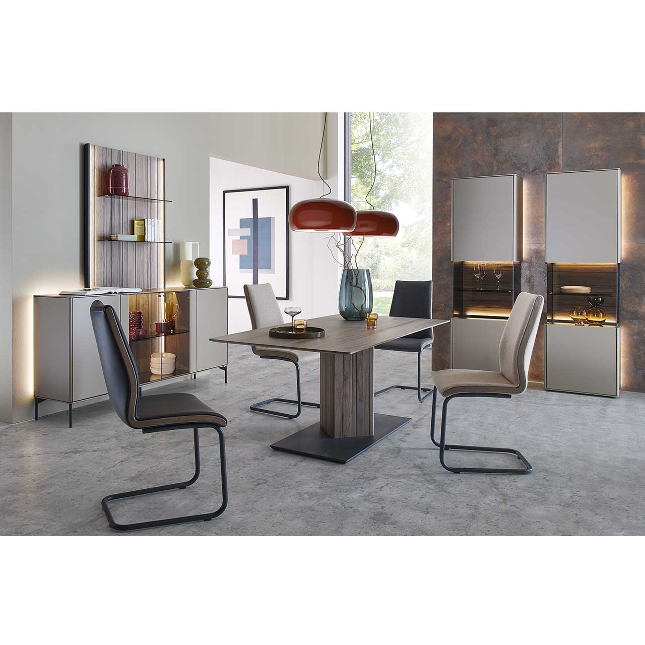 Modern eingerichtetes Esszimmer mit rechteckigem Tisch aus massiver Altholzbuche Uyaa und vier Freischwingern mit hellem Lederbezug. Rechts an der Wand zwei beleuchtete Standvitrinen mit  sandfarbenen Lackfronten. Links das passende Sideboard mit Paneel.