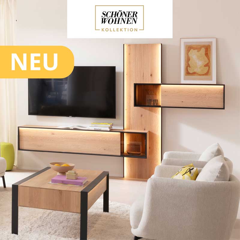 Hartmann YOLA - Wohnzimmermöbel aus massiver Kerneiche Natur sandgestrahlt kombiniert mit Metall anthrazit. Ambientebild zeigt beleuchtetes Wandpaneel mit Hängevitrine und Lowboard in Metall eingefasst. Davor passender rechteckiger Holz-Couchtisch.